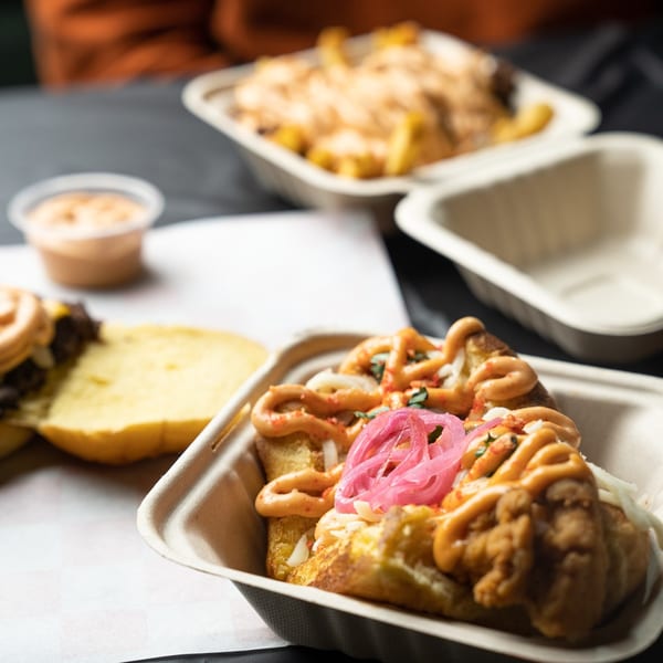 Bricked Burgers' fried chicken sandwich with pickled onions and sauce, with fries and a burger in the background.